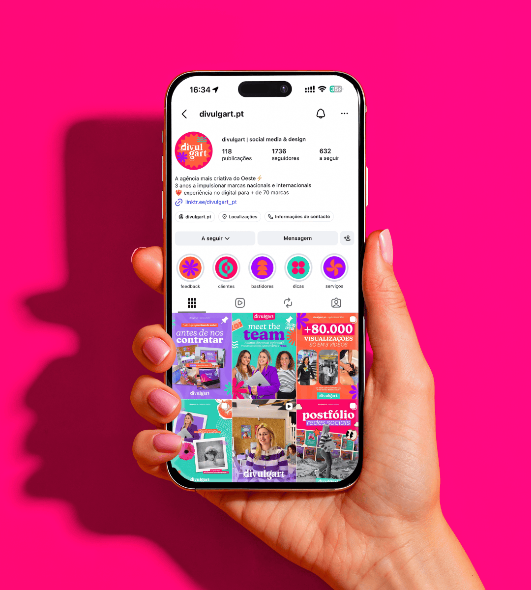 Mão a segurar um smartphone com o perfil de Instagram da Divulgart, sobre um fundo cor-de-rosa.