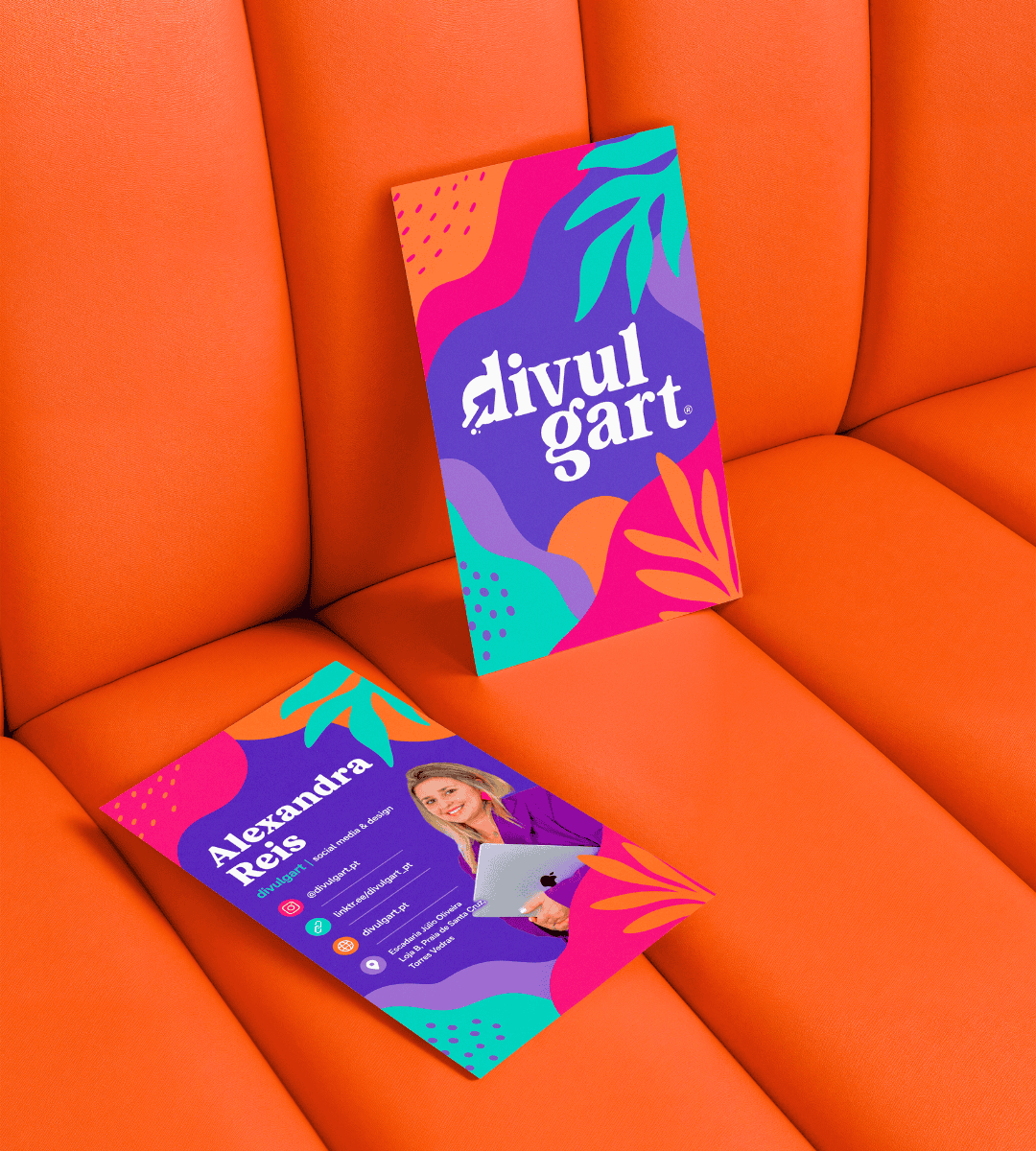 Mockup com a frente e o verso dos cartões de visita da Divulgart, sobre um sofá roxo, com o logótipo, os contactos e a fotografia de Alexandra Reis.